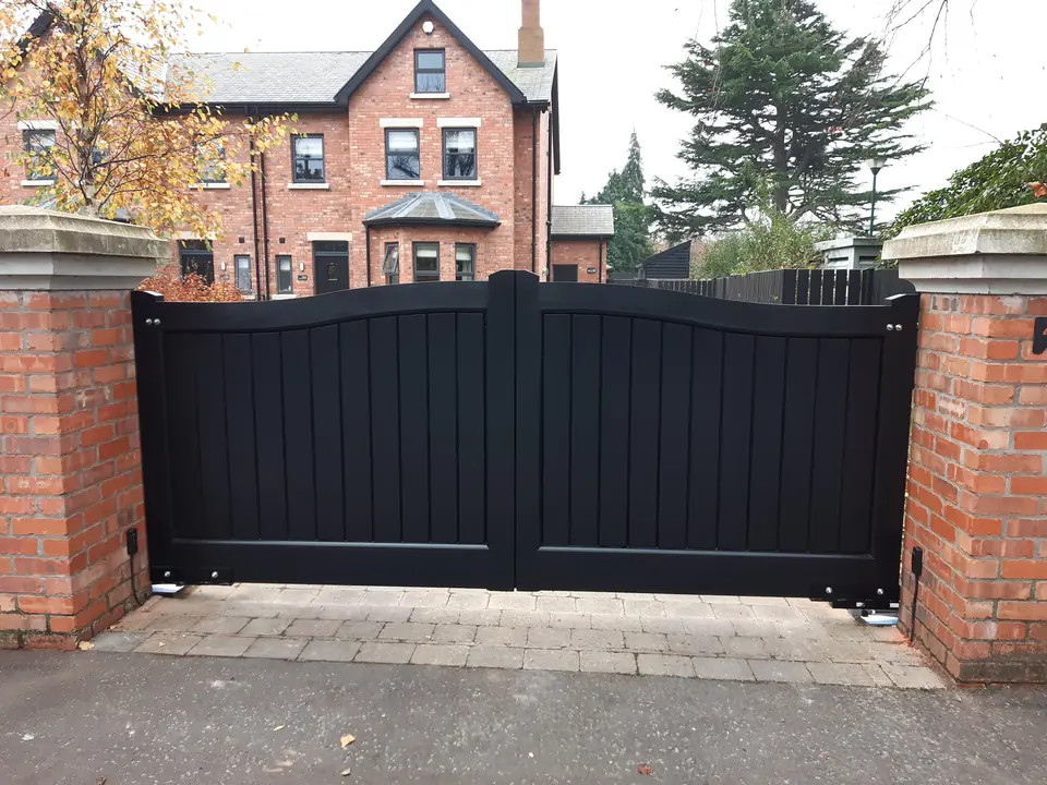Black arched driveway gates between brick pillars